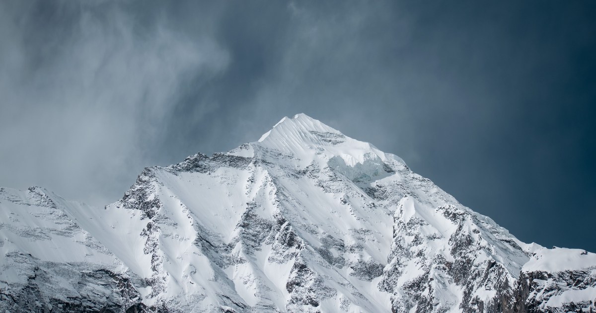 A steep snow-plastered peak under a dark stormy sky