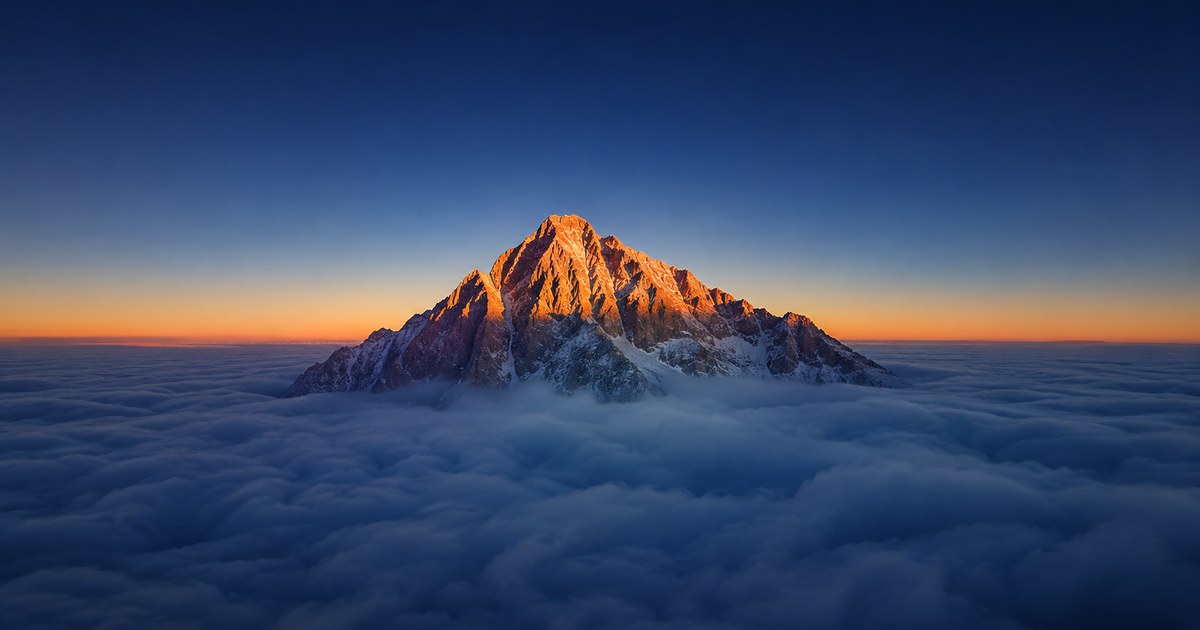 A single immense snow-covered summit rising alone above layered ridgelines at dusk