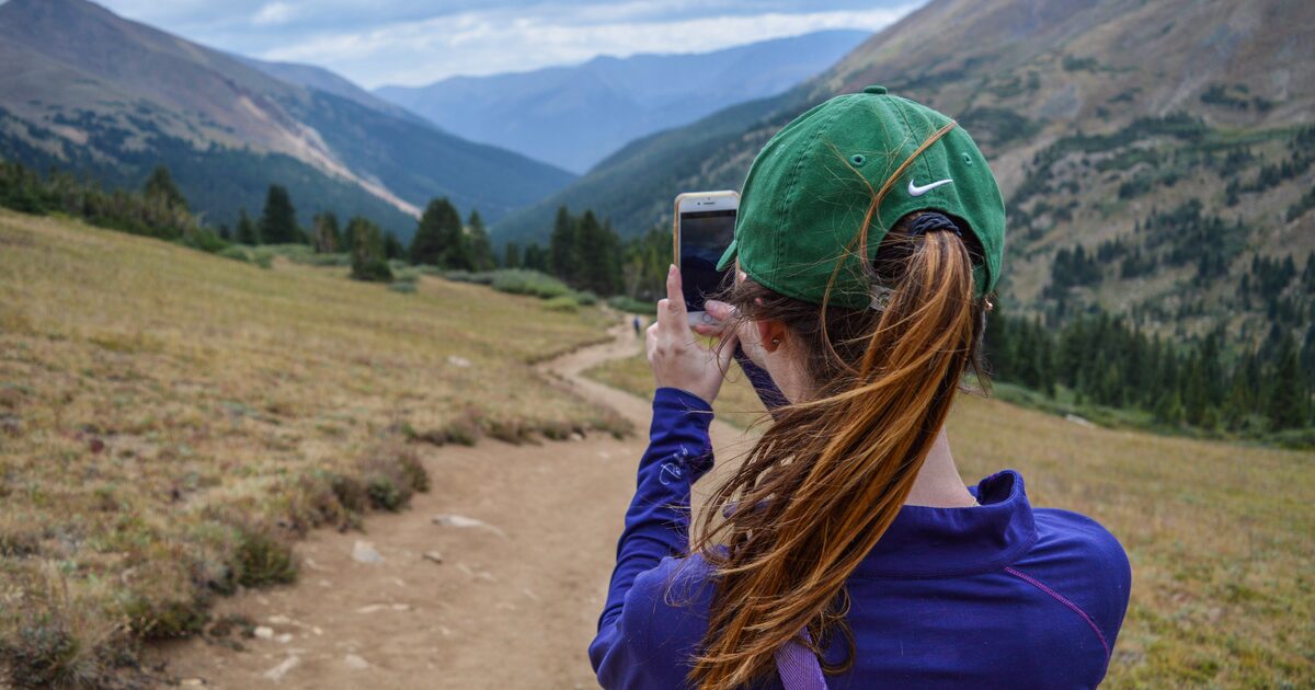 A hiker photographing a mountain valley with a smartphone