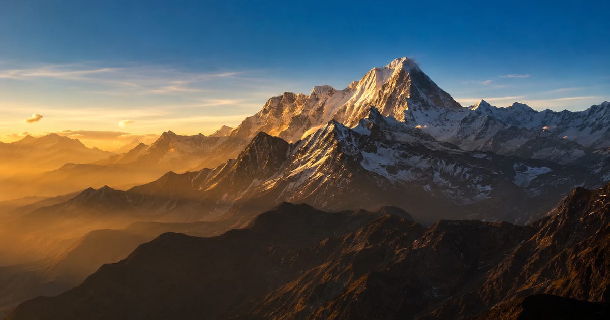 A dramatic snow-capped mountain range silhouetted at golden hour