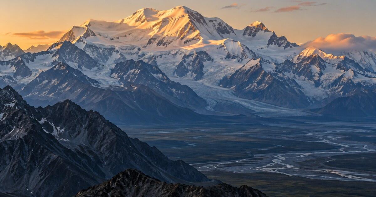 An anonymous glaciated mountain massif lit gold at sunset above a wide valley of braided rivers