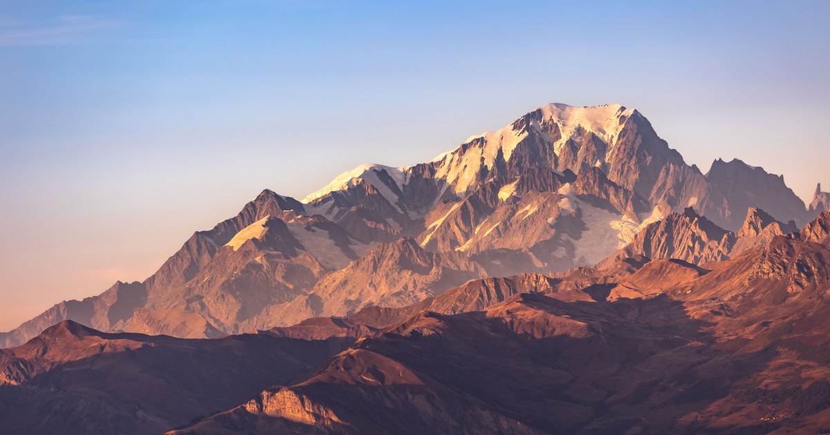 A broad mountain massif with several distinct summits sharing one base at sunrise